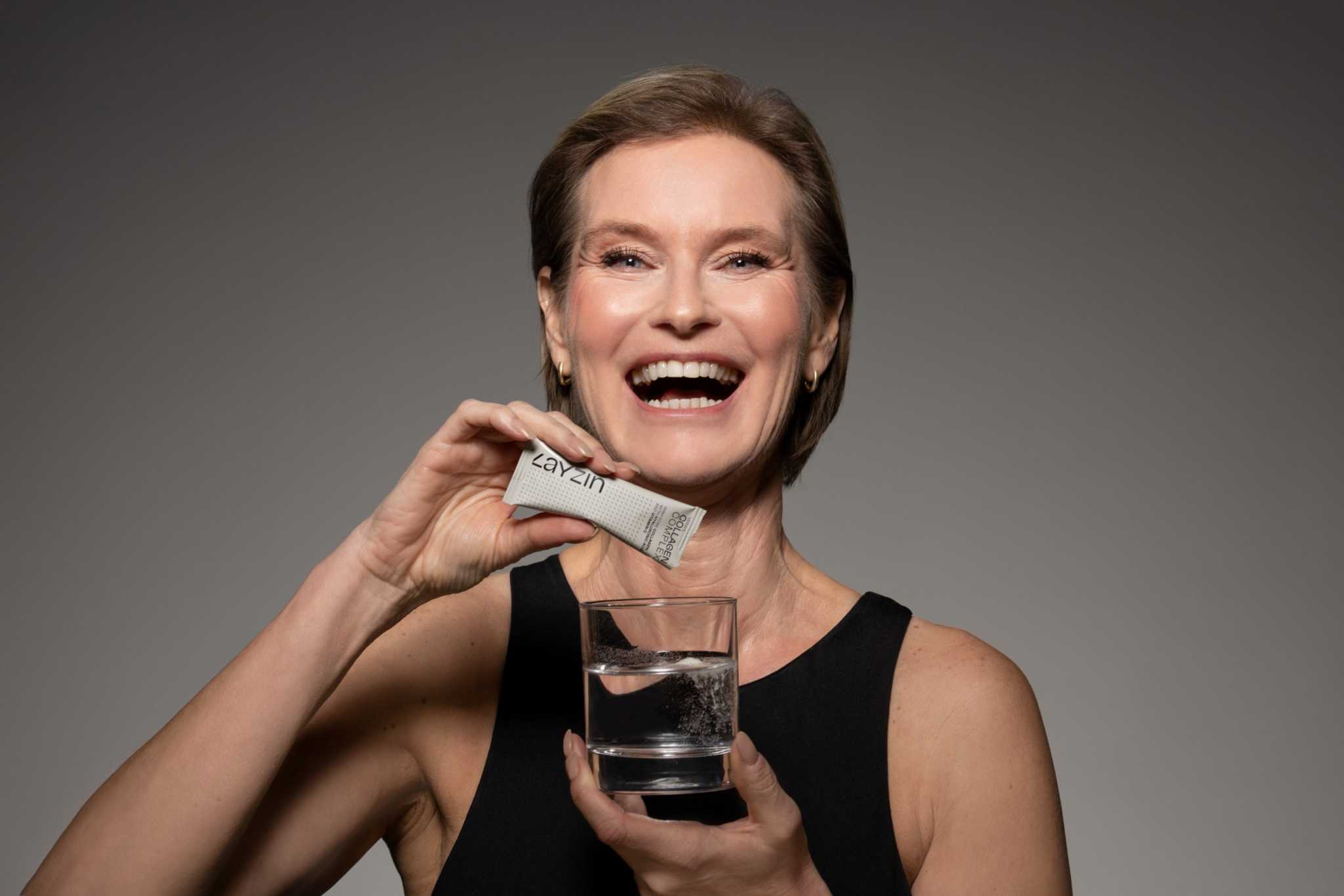 Vrouw glimlachend met LAYZIN Collageen sachet en glas water voor huidverjonging en haar- en nagelversterking